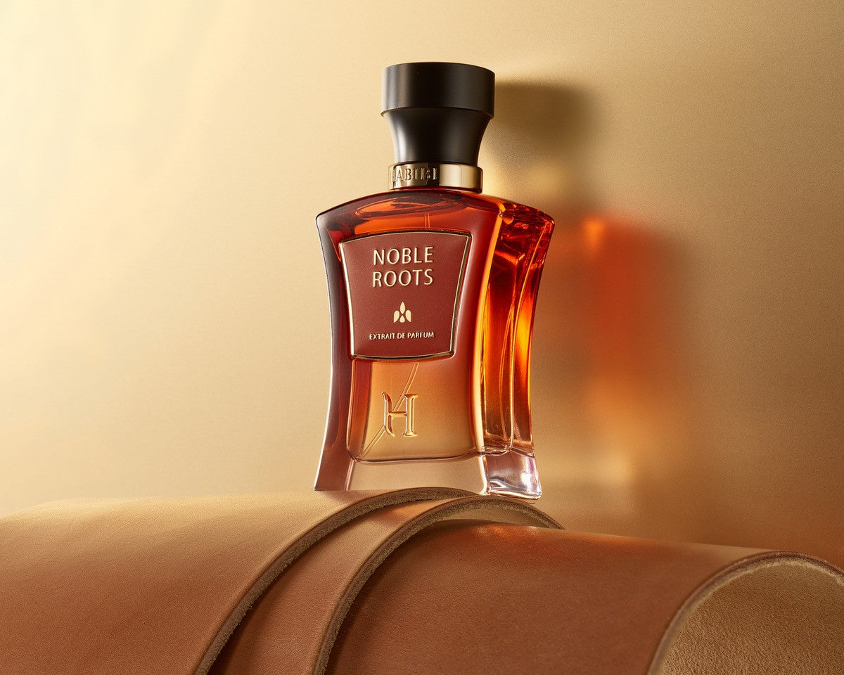 Noble Roots Extrait de Parfum by HABIBI New York, amber-red glass bottle with black cap resting on tan leather.