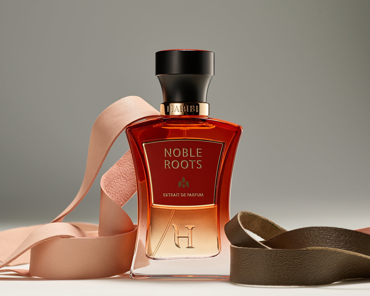 Noble Roots Extrait de Parfum by HABIBI New York, amber-red glass bottle with black cap resting on tan leather.