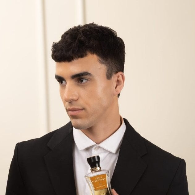 A man in a black suit holding a HABIBI bottle