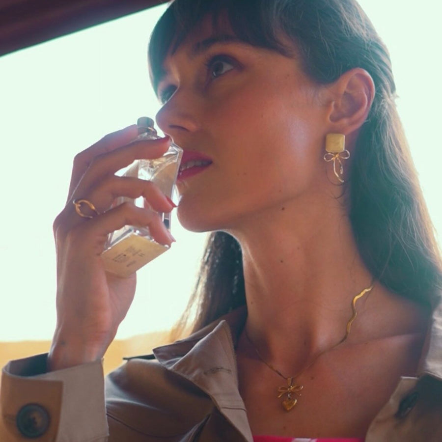 A woman in a trench coat smelling fragrance on her wrist