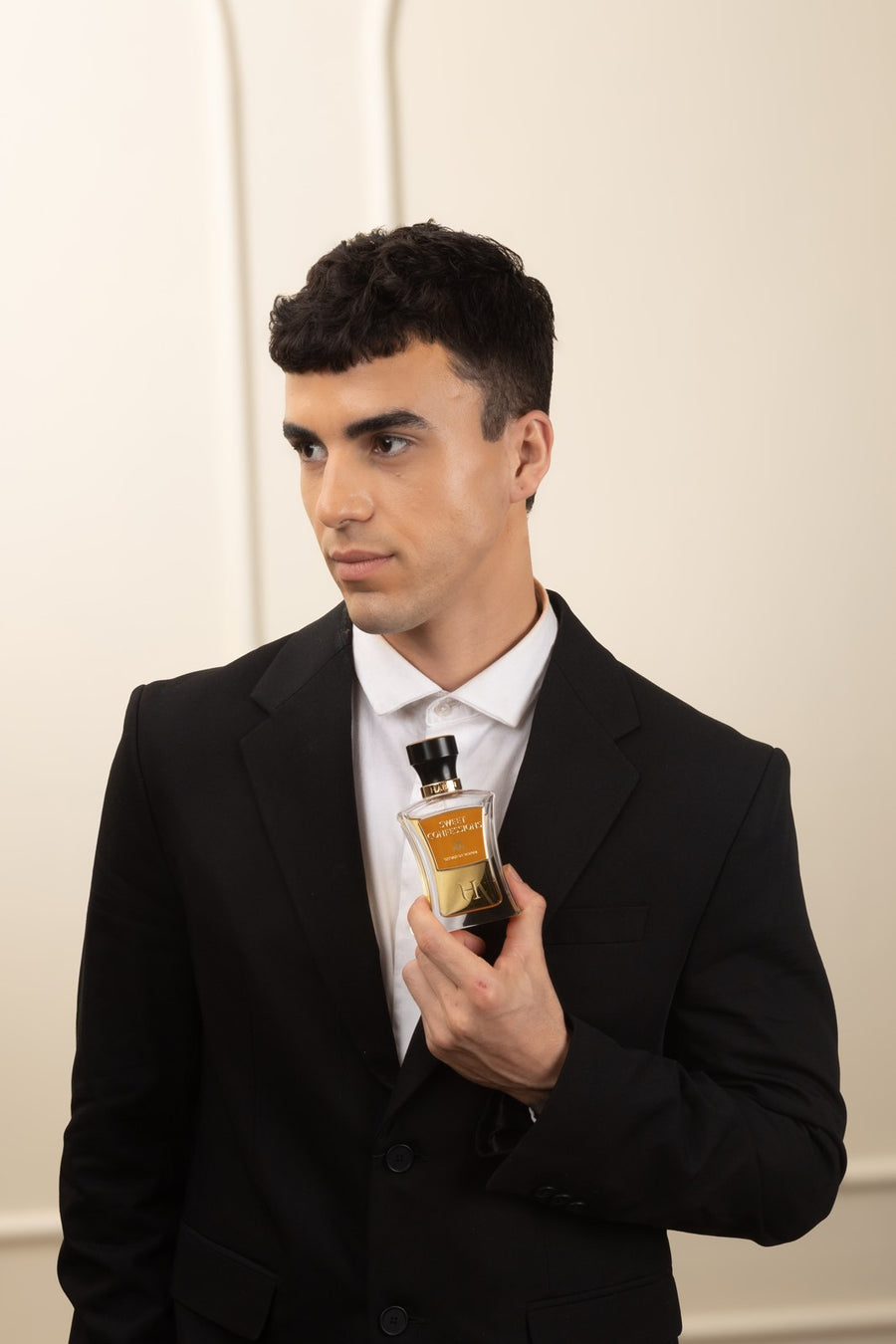 A man in a black suit holding a HABIBI bottle